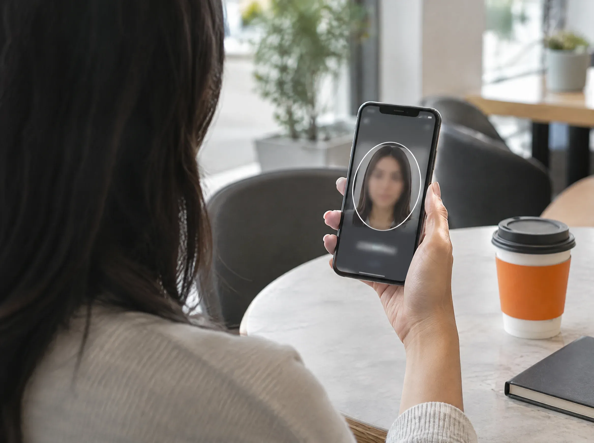 Mulher em café segurando celular com moldura de verificação facial na tela